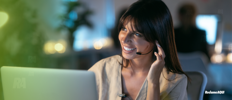 Mulher sorrindo atrás de um notebook e utilizando um fone de ouvido.
