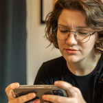 onsumidora preocupada olhando celular, verificando site falso na Black Friday 2025